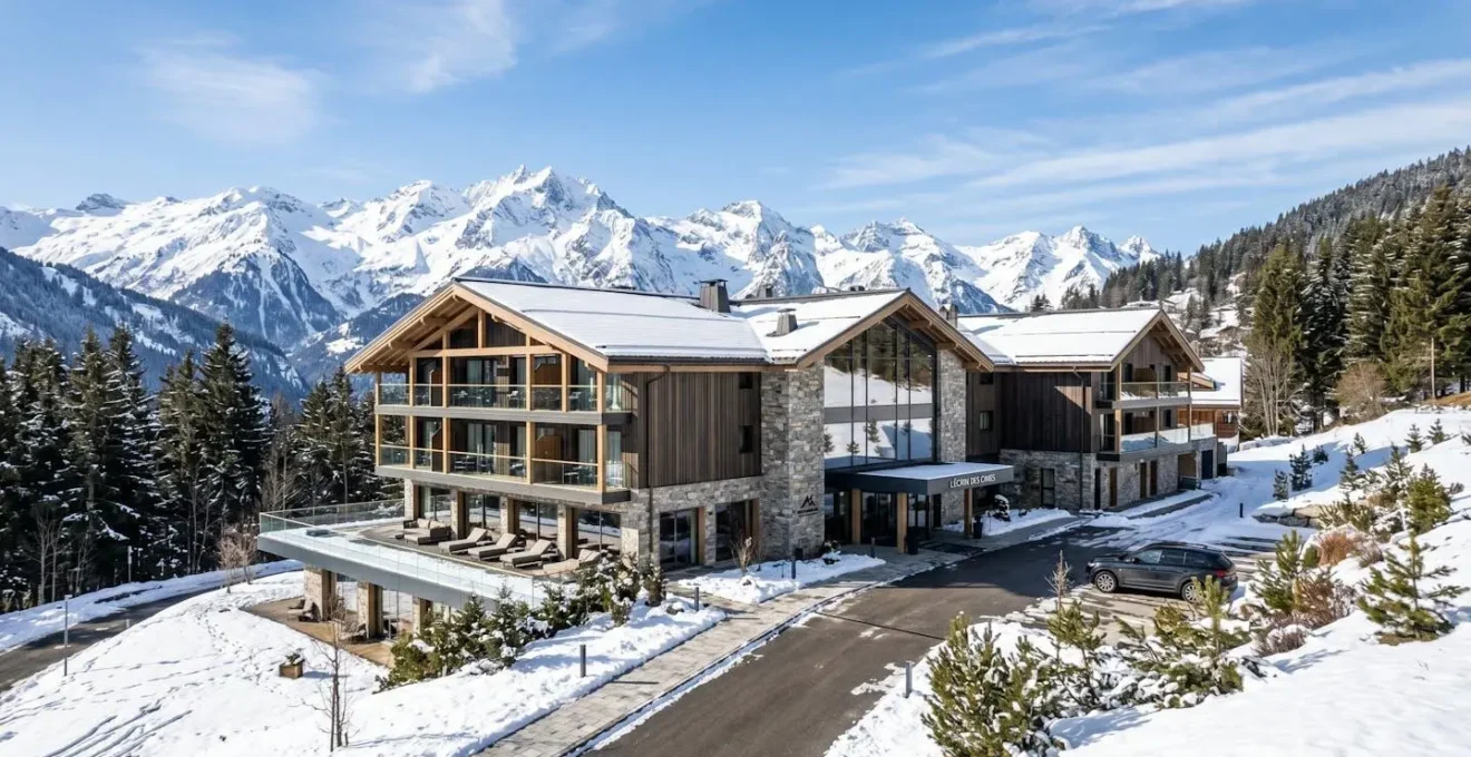 Vue extérieure d'un hôtel de style chalet contemporain aux lignes épurées, niché dans un environnement montagnard enneigé sous un ciel bleu lumineux